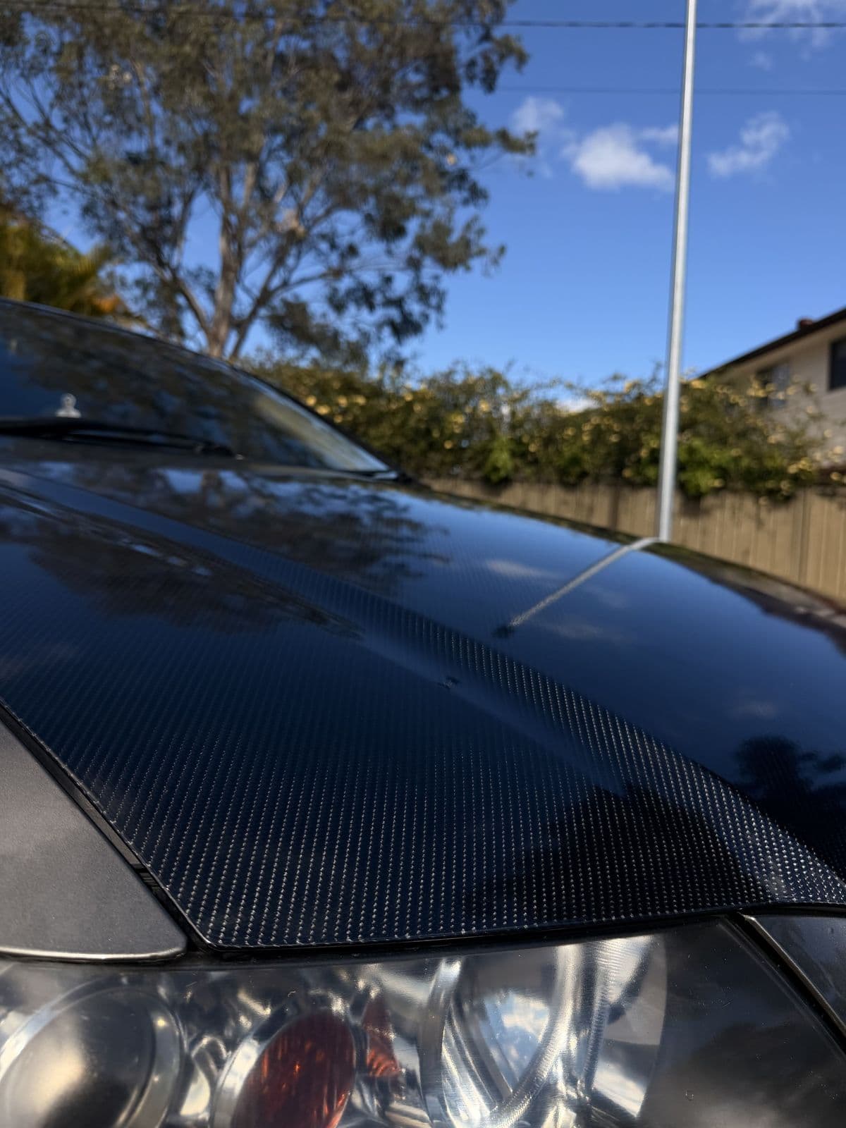 Carbon fibre vinyl wrapped bonnet next to the headlight, fitted cleanly to the panel edge